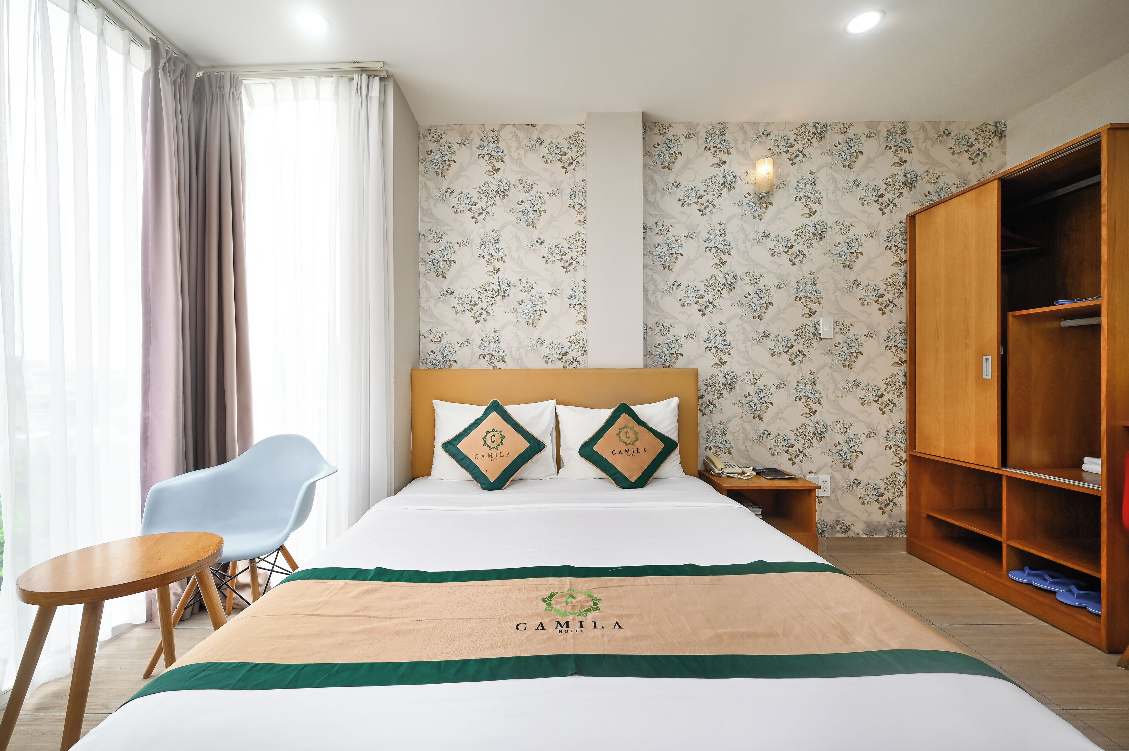 Habitació d'hotel ordenada amb un llit, una cadira, un armari de fusta i una taula de nit.