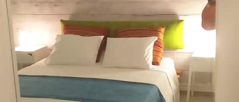 A bedroom with a wooden headboard, a bed with white and blue bedding, and a green rug.