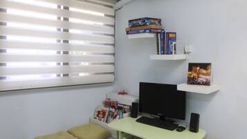 Una habitación pequeña y bien iluminada con un escritorio, computadora y estanterías llenas de libros y un marco de fotos.