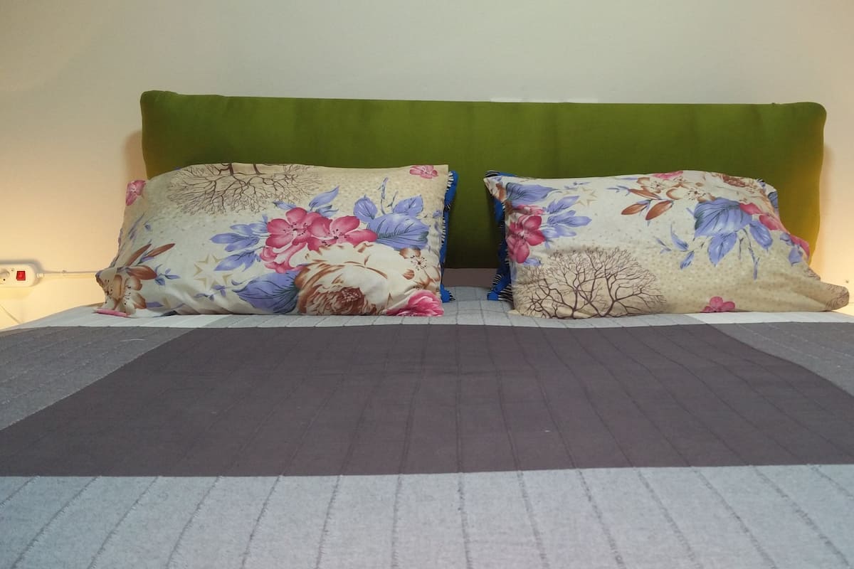 Ein Bett mit einem grünen Kopfteil, zwei Kissen mit Blumenmuster und einer grau-weißen Streifenauflage.
