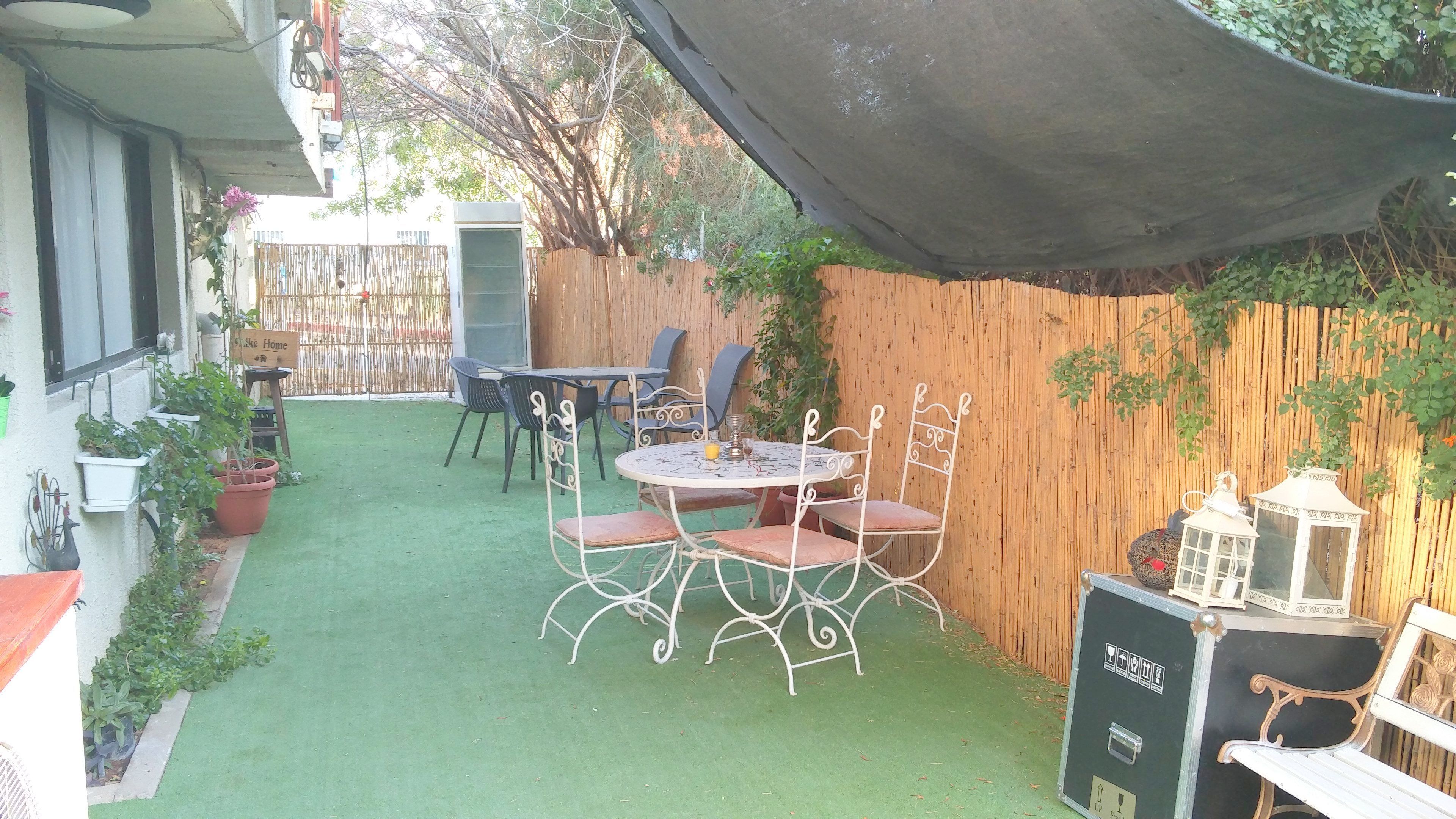 A patio with a round table and chairs, surrounded by potted plants and a bamboo fence.