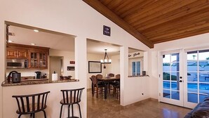 Une cuisine moderne avec des meubles en bois, un coin repas agrémenté d’un lustre, et une vue sur une piscine à travers des portes vitrées.