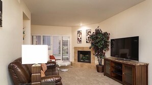 Un salon avec un canapé en cuir marron, une lampe blanche, un téléviseur à écran plat, une cheminée et deux œuvres d’art accrochées au mur.