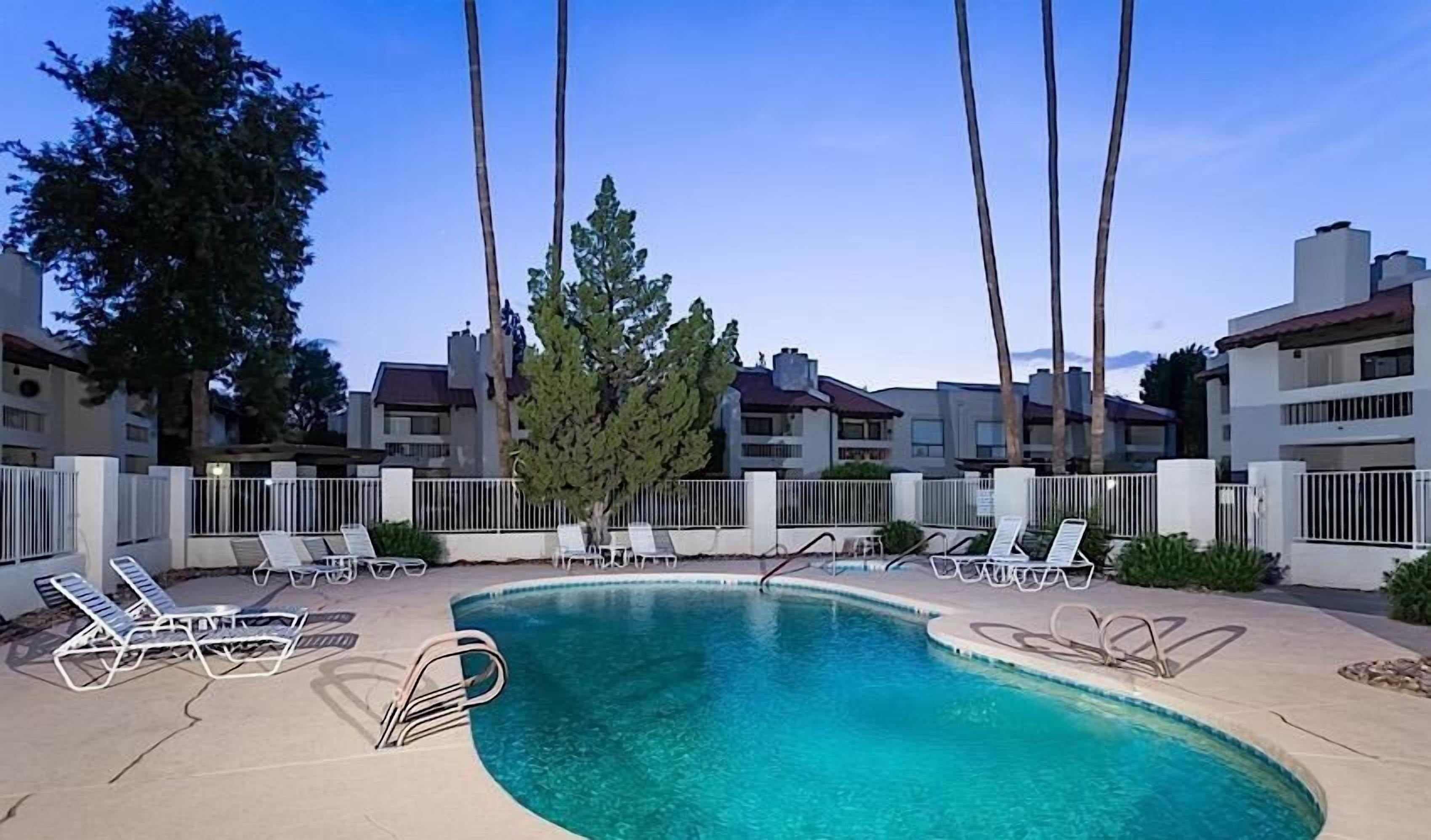 A swimming pool with lounge chairs and a tree in the center, surrounded by apartment buildings.