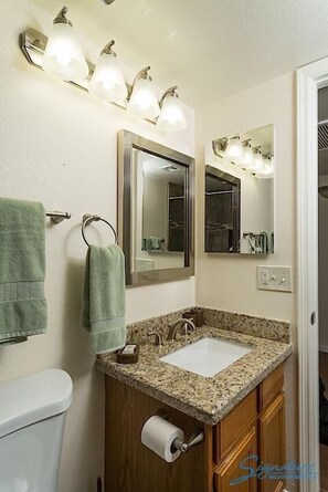Une salle de bain avec un lavabo doté d’un plan de travail en granit, deux miroirs, un porte-serviettes et des toilettes.
