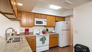 Une cuisine avec des meubles de rangement en bois, une cuisinière blanche, un four à micro-ondes, un réfrigérateur, un évier et une poubelle.