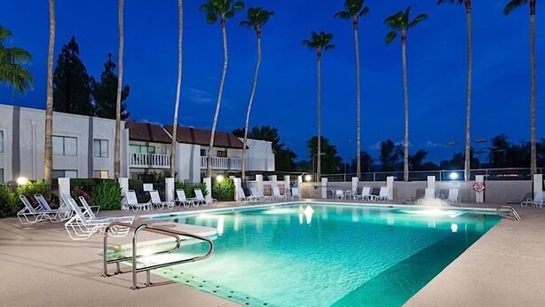 Une piscine avec des chaises longues et des palmiers, au crépuscule.