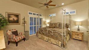 Quarto com cama, cadeira, mesa de cabeceira, ventilador de teto e janela com persianas.