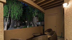 Ett takförsett utomhusområde med sittplatser, möbler av rotting och utsikt över en trappa som leder upp till en byggnad.