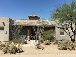Un edificio con techo de tejas, un patio con cactus y un cielo azul despejado.