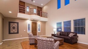 Un salon spacieux avec un plafond haut, un balcon et une grande fenêtre équipée de stores.