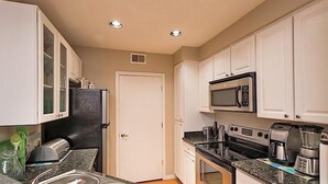 A compact kitchen with white cabinets, a black refrigerator, a microwave, a stove, and a coffee maker. - Phoenix Palms By Signature Vacation Rentals (Phoenix)