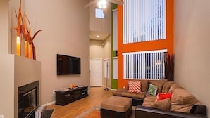 A modern living room with a fireplace, a flat-screen TV, and a large window with blinds. - Phoenix Palms By Signature Vacation Rentals (Phoenix)