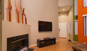 A living room with a fireplace, a flat-screen TV mounted on the wall, and a wooden floor. - Phoenix Palms By Signature Vacation Rentals (Phoenix)