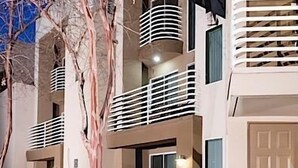 A multi-story building with balconies, a tree, and a well-lit entrance. - Phoenix Palms By Signature Vacation Rentals (Phoenix)