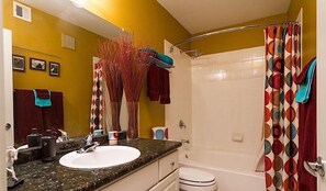 A bathroom with a white sink, a toilet, and a shower with colorful curtains. - Phoenix Palms By Signature Vacation Rentals (Phoenix)