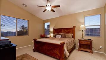 A bedroom with a wooden bed, two bedside tables, a ceiling fan, and large windows.