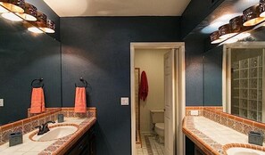 A bathroom with dark walls, two sinks with patterned countertops, and a mirror with lights. - Peak of Perfection By Signature Vacation Rentals (Tucson)