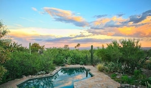 A pool surrounded by lush greenery and a desert landscape with a sunset in the background. - Peak of Perfection By Signature Vacation Rentals (Tucson)