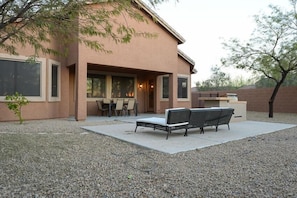Une maison dotée d’un patio comprenant une table et des chaises, un banc et un petit arbre.