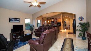 A spacious living room with a large brown leather sofa, a flat-screen TV, and a ceiling fan. - Scenic Spectacular By Signature Vacation Rentals (Oro Valley)