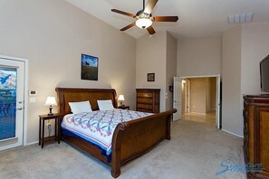 A bedroom with a wooden bed, a ceiling fan, a nightstand, a dresser, and a door leading to another room. - Scenic Spectacular By Signature Vacation Rentals (Oro Valley)