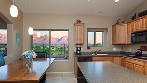 A modern kitchen with wooden cabinets, a large island, and a view of mountains through the sliding glass door. - Scenic Spectacular By Signature Vacation Rentals (Oro Valley)