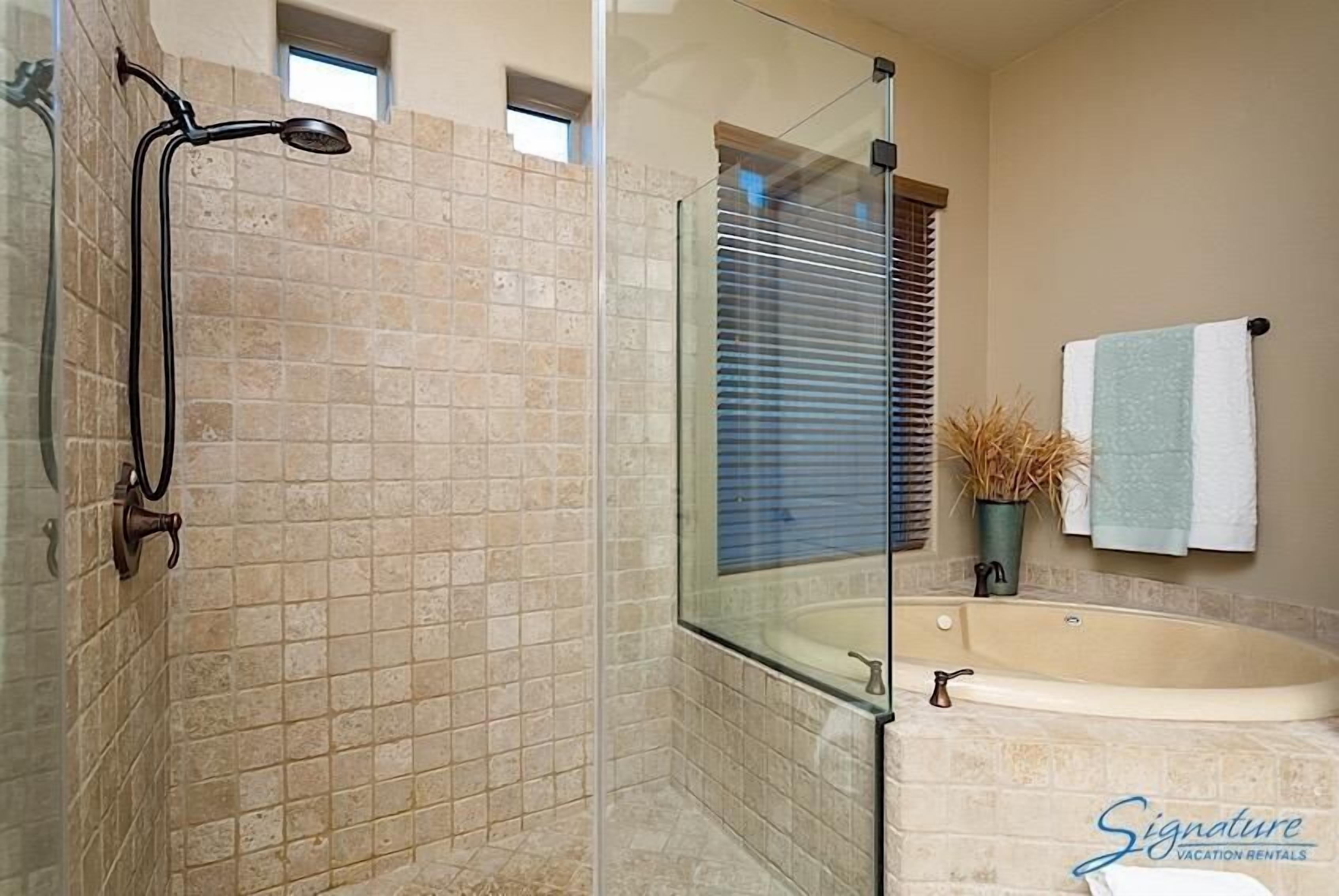 A bathroom with a glass-enclosed shower, a bathtub, and a window with blinds.