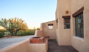 A building with a stucco exterior, a small window with bars, and a fire pit area. - Saguaro Serenity By Signature Vacation Rentals (Tucson)