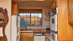 Une cuisine avec des meubles de rangement en bois, un lave-vaisselle, une cuisinière et une fenêtre donnant sur des collines.
