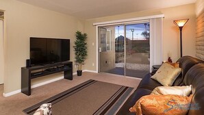 A living room with a flat-screen TV, a sofa, a coffee table, a potted plant, and a sliding glass door leading to a patio. - Parktopia By Signature Vacation Rentals (Scottsdale)