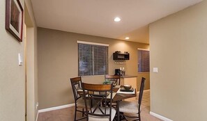 A dining area with a table and four chairs, a kitchen area with a microwave, and a window with blinds.
