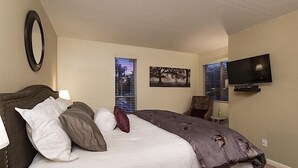 A bedroom with a bed, a television, and two windows with blinds. - Parktopia By Signature Vacation Rentals (Scottsdale)