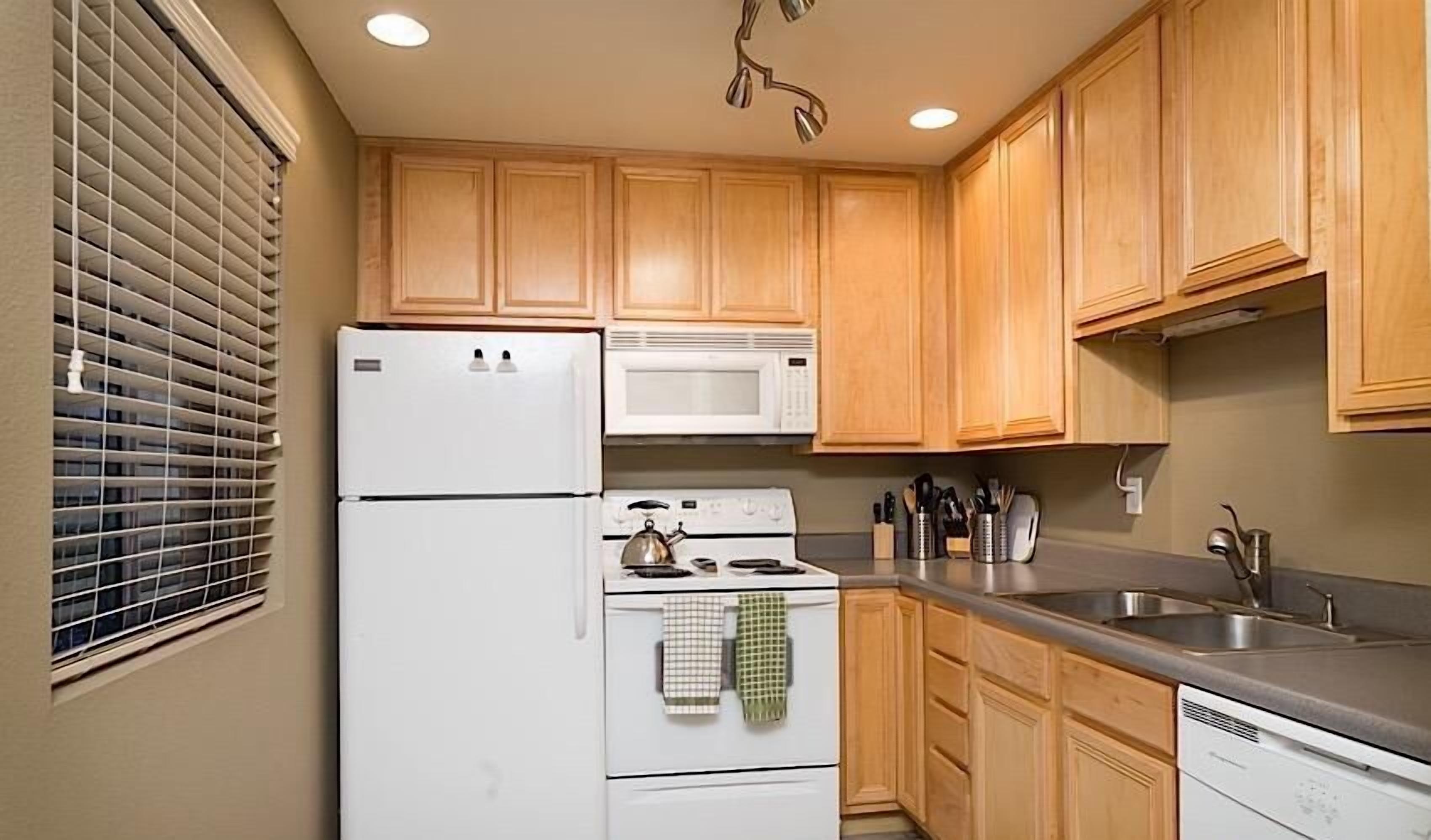 Una cocina compacta con armarios de madera, un refrigerador blanco, un microondas, una estufa y un lavavajillas.