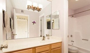 A bathroom with a large mirror, a sink, a shower, and a door leading to another room.