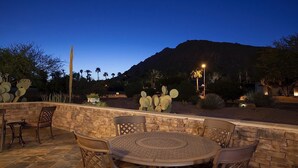 An outdoor patio with a round table and chairs, surrounded by a stone wall, with cacti and palm trees in the background. - Paradise Retreat - PV622 By Signature Vacation Rentals (Scottsdale)