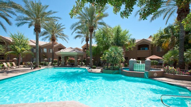 A swimming pool surrounded by palm trees and a building with a tiled roof. - Paradise Found By Signature Vacation Rentals (Scottsdale)