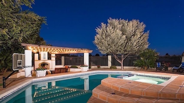 A swimming pool with a hot tub, a pergola with string lights, outdoor furniture, and a large tree. - Palm Valley By Signature Vacation Rentals (Goodyear)