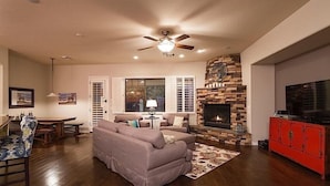 A living room with a stone fireplace, a ceiling fan, and a television. - Palm Valley By Signature Vacation Rentals (Goodyear)