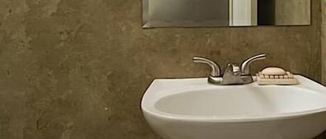 Une salle de bain avec un lavabo sur colonne blanc, trois appliques murales et un miroir au-dessus du lavabo.