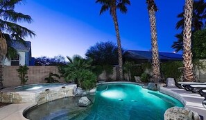 A swimming pool with a curved design, surrounded by palm trees and a stone wall. - Painted Horizon By Signature Vacation Rentals (Scottsdale)
