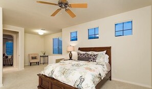 A bedroom with a bed, a ceiling fan, two windows, a nightstand, a lamp, and a chair. - Overlook Chalet By Signature Vacation Rentals (Scottsdale)