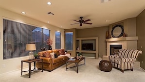 A living room with a brown leather sofa, a striped armchair, a coffee table, a fireplace, and a ceiling fan. - Overlook Chalet By Signature Vacation Rentals (Scottsdale)