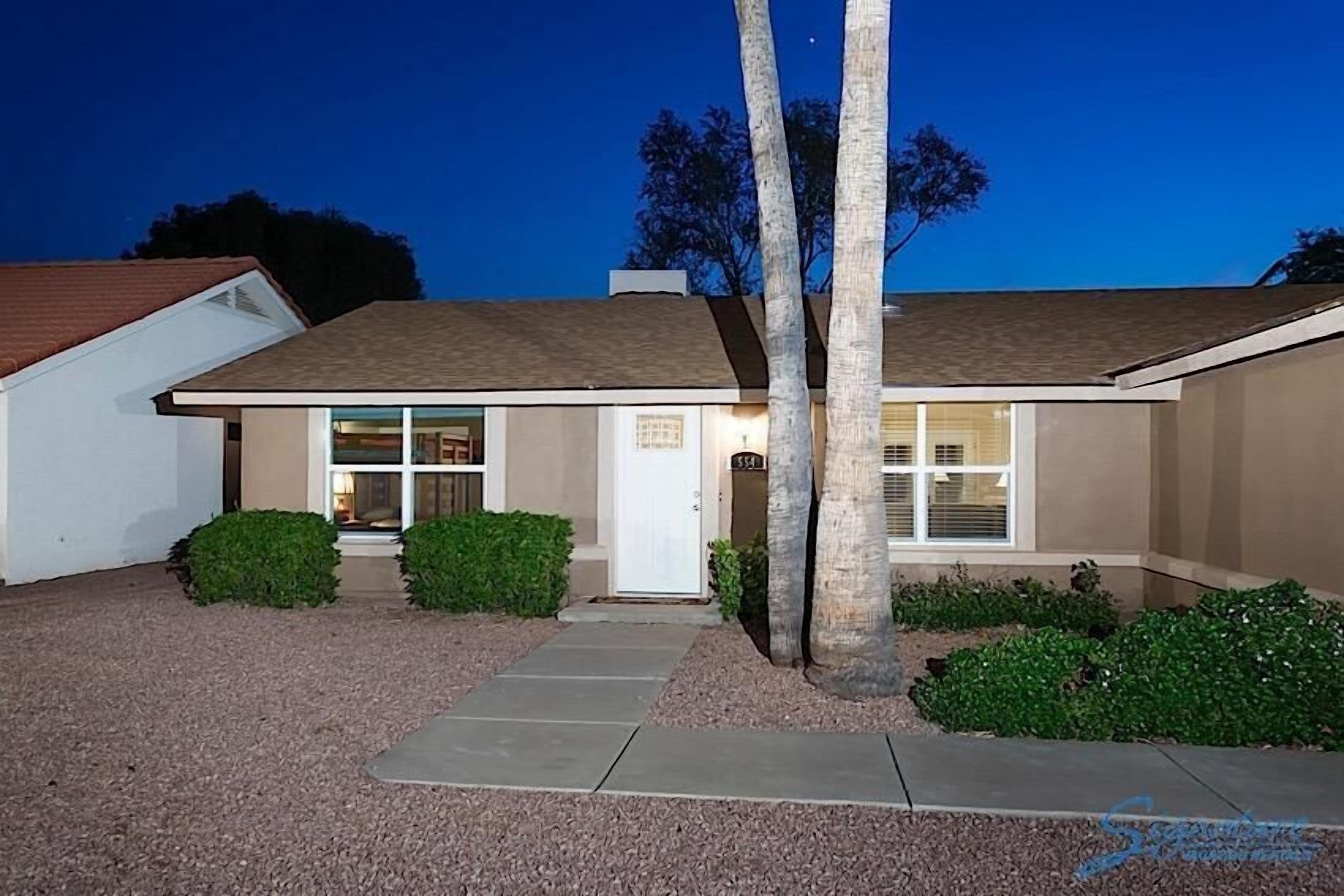 A single-story house with a front entrance, a visible garage door, and a well-maintained lawn with trimmed bushes.