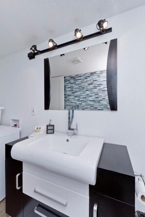 A modern bathroom with a white sink, dark cabinetry, a large mirror, and a mosaic tile backsplash. - Old School By Signature Vacation Rentals (Scottsdale)