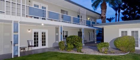 A two-story building with a covered patio area, a palm tree, and a well-maintained lawn.