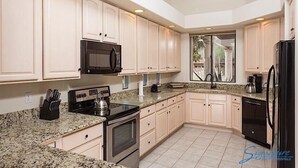 A modern kitchen with white cabinets, granite countertops, stainless steel appliances, and a large window providing natural light. - Northstar By Signature Vacation Rentals (Scottsdale)