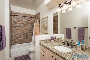 A bathroom with a stone wall, a bathtub, a white sink, and a vanity with a mirror.