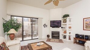 A spacious living room with a large TV, a fireplace, and a ceiling fan. - Northstar By Signature Vacation Rentals (Scottsdale)