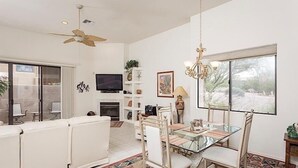 A spacious living room with a glass dining table, white sofas, a ceiling fan, a fireplace, and a large window offering a view of the outdoors. - Northstar By Signature Vacation Rentals (Scottsdale)
